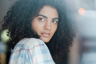 Young woman with curly hair looking through glass - KNSF09228