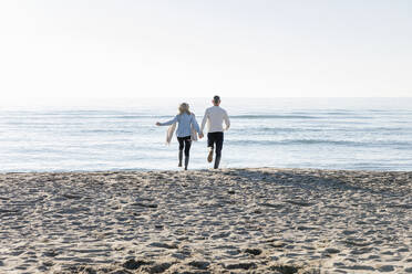 Man and woman running towards sea at beach - EIF02563