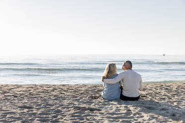 Mann mit Arm um Frau sitzt zusammen im Sand am Strand - EIF02564