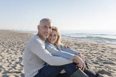 Happy couple sitting together at beach - EIF02567