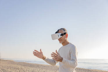 Mann gestikuliert mit Virtual-Reality-Headset am Strand - EIF02576