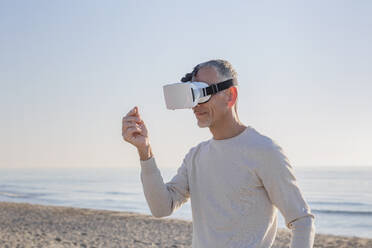 Mann mit Virtual-Reality-Headset gestikuliert am Strand - EIF02577