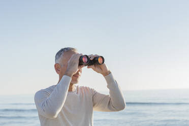 Mann schaut durch ein Fernglas am Strand - EIF02582