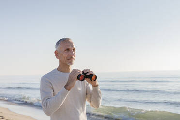 Man holding binoculars standing at beach - EIF02583