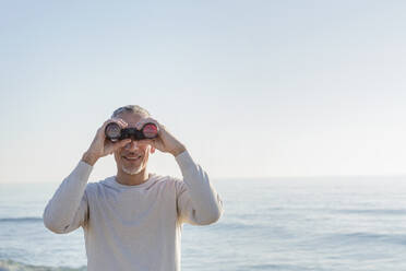 Lächelnder Mann schaut durch ein Fernglas - EIF02585