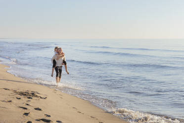 Mann, der eine Frau am Strand huckepack nimmt - EIF02611