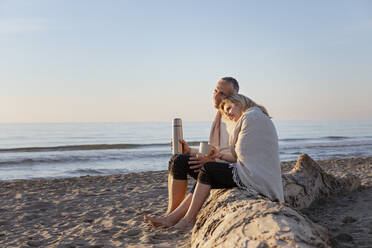 Couple sitting on tree log enjoying sunset at beach - EIF02619