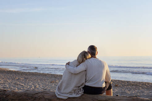 Mann mit Arm um Frau schaut auf Sonnenuntergang am Strand - EIF02622