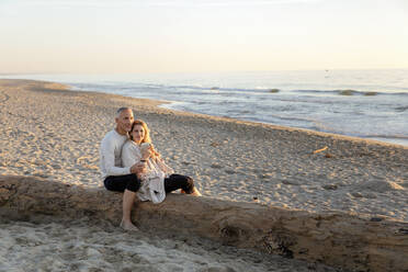 Frau mit Teetasse lehnt sich an einen Mann, der am Strand sitzt - EIF02625