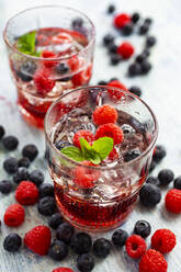 Zwei Gläser Gin Tonic mit Minze, Eiswürfeln und rohen Beeren - GIOF14361