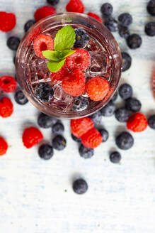 Ein Glas Gin Tonic mit Minze, Eiswürfeln und rohen Beeren - GIOF14362