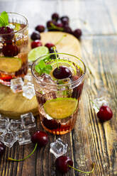 Glass of refreshing drink with lime, mint, raw cherries and ice cubes - GIOF14376