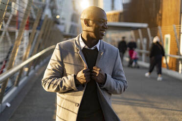 Smiling businessman holding long coat standing on bridge - GIOF14381