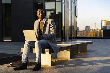 Businessman with laptop sitting on bench - GIOF14389