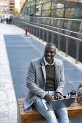 Contemplative businessman with laptop sitting on bench - GIOF14390