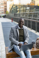Arbeitender Mann mit Laptop auf einer Bank sitzend - GIOF14391