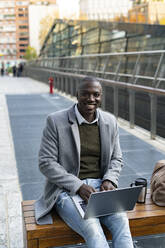 Working man with laptop sitting on bench - GIOF14391