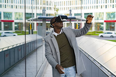 Businessman gesturing wearing virtual reality headset near glass wall in city - GIOF14402