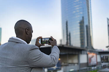 Businessman photographing buildings through smart phone in city - GIOF14436