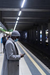 Geschäftsmann mit Gesichtsschutzmaske und Smartphone am Bahnhof - GIOF14438