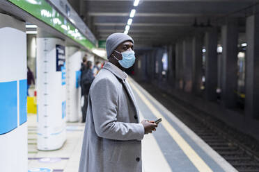 Nachdenklicher Geschäftsmann mit Gesichtsschutzmaske auf dem Bahnhof - GIOF14439