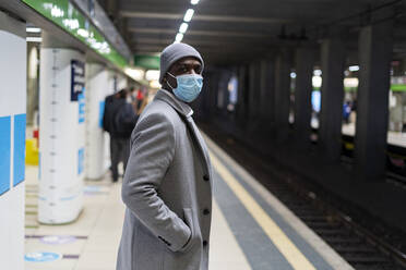 Geschäftsmann mit Hand in der Tasche und Gesichtsschutzmaske auf einem Bahnhof - GIOF14440