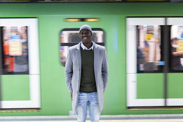 Lächelnder Geschäftsmann vor einem Zug im Bahnhof stehend - GIOF14443