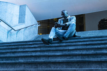 Businessman using smart phone sitting on steps in subway - GIOF14450