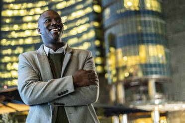 Smiling businessman with arms crossed in city at night - GIOF14460