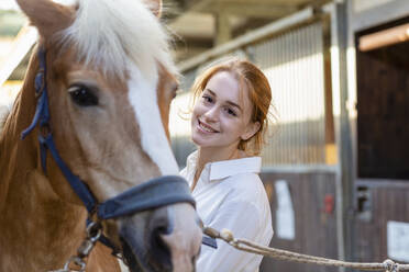 Lächelnde Frau betrachtet ein Pferd im Stall - EIF02638