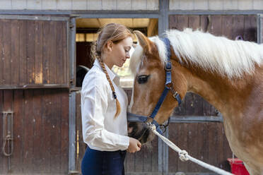 Junge Frau mit Pferd im Stall stehend - EIF02639