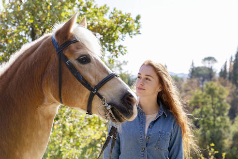 Junge Frau steht bei einem Pferd an einem sonnigen Tag - EIF02654
