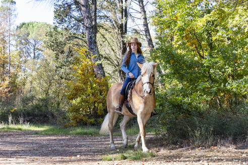 Frau trägt Hut beim Reiten auf einer Wiese - EIF02660