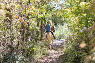 Junge Frau schaut über die Schulter beim Reiten im Wald an einem sonnigen Tag - EIF02666