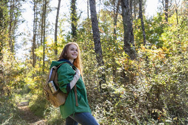 Lächelnde Frau mit Rucksack schaut beim Wandern im Wald weg - EIF02672