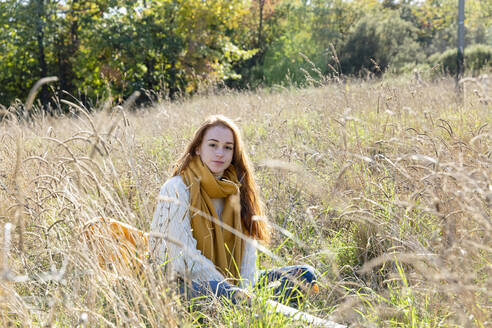 Junge Frau sitzt an einem sonnigen Tag im Gras - EIF02695