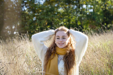 Smiling woman with hand in hair standing amidst grass - EIF02699