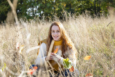 Happy woman sitting amidst grass on sunny day - EIF02700