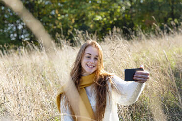Junge Frau nimmt Selfie auf Smartphone im Gras - EIF02701
