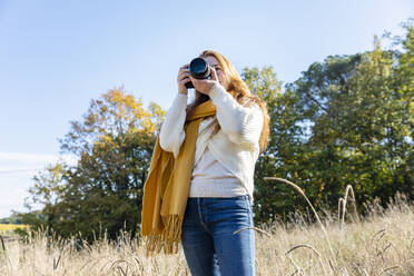 Young woman photographing through camera while standing in grass - EIF02703