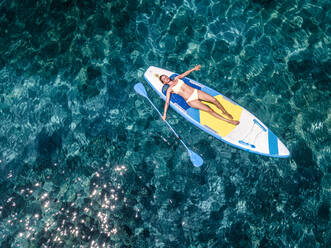 Reife Frau im Bikini entspannt sich auf Paddleboard im Meer - HMEF01336