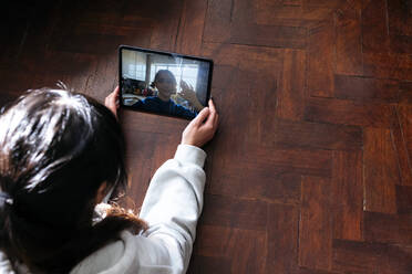 Junge Frau im Gespräch mit einem Freund, der bei einem Videogespräch mit einem Tablet-PC auf einem Hartholzboden winkt - ASGF01912