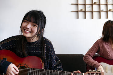 Lächelnde Frau spielt Gitarre mit einem Freund zu Hause - ASGF01922