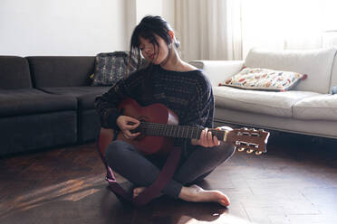 Woman playing guitar on floor in living room - ASGF01925