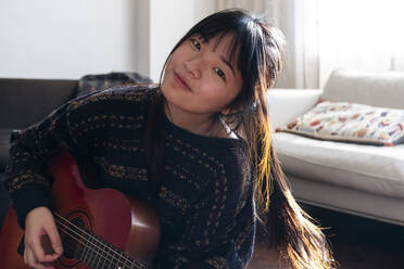 Lächelnde junge Frau, die zu Hause Gitarre spielt - ASGF01926