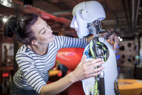 Lächelnder Techniker mit Arm um menschlichen Roboter in der Werkstatt - WESTF24764