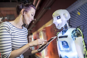 Technician programming human robot through tablet PC at workshop - WESTF24766