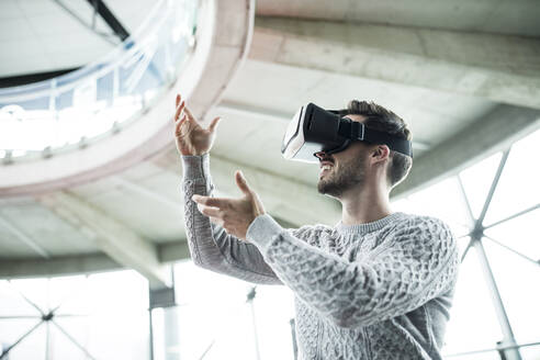 Lächelnder Technikentwickler mit Virtual-Reality-Headset gestikuliert beim Workshop - WESTF24797