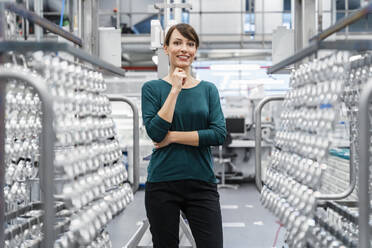 Smiling businesswoman with hand on chin at industry - DIGF17066