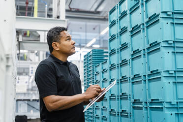 Warehouse worker inspecting blue crates in industry - DIGF17091